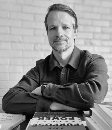 a black and white photo of a white man with folded arms starting straight into the camera